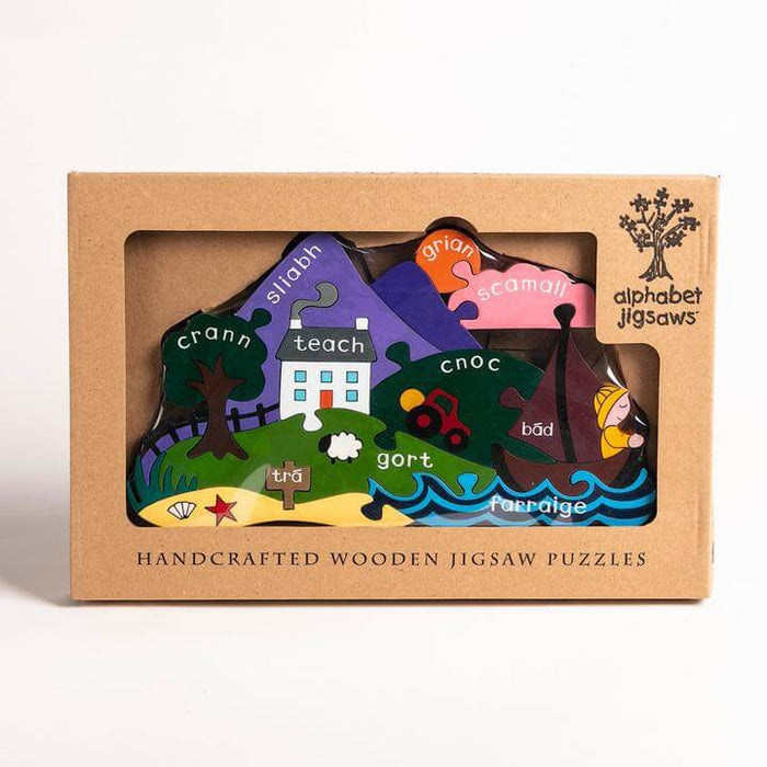 Colorful wooden landscape puzzle in a box with pieces labeled in Irish, featuring a mountain, house, and sailboat.