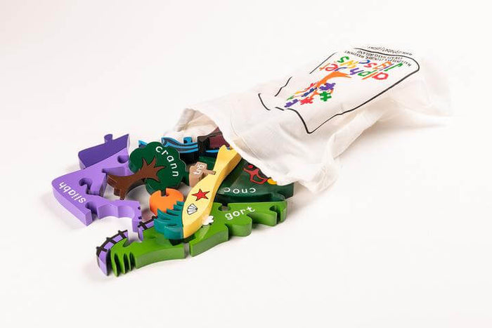 Colorful wooden jigsaw pieces with Irish text spilling out of a white Alphabet Jigsaws drawstring cotton bag.