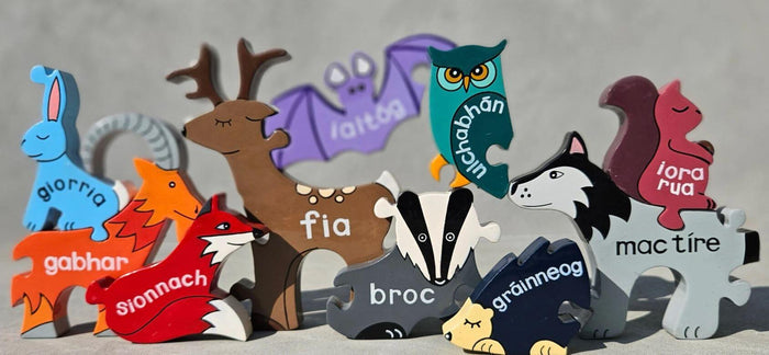 Colorful wooden puzzle pieces shaped like Irish animals like a deer and fox, each labeled with its name in Irish.
