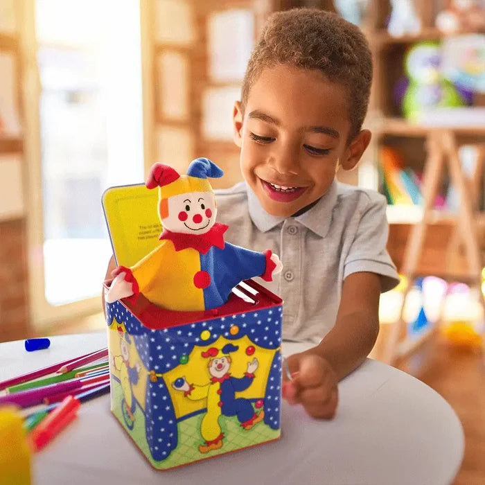 Smiling boy playing with a colorful plush clown popping out of a circus-themed metal jack-in-the-box.