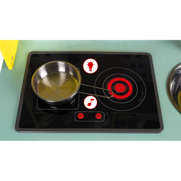 Close-up of a black toy stovetop with a red glowing burner, silver pan, and buttons for lights and sounds.