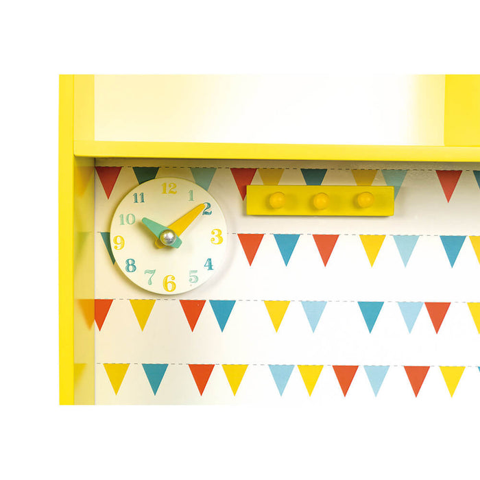 Detail of a yellow toy kitchen with a wooden clock, three knobs, and colorful triangle bunting.