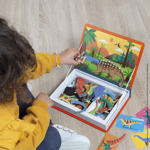 Child playing with magnetic dinosaur pieces on a prehistoric background inside an orange book-shaped toy box.