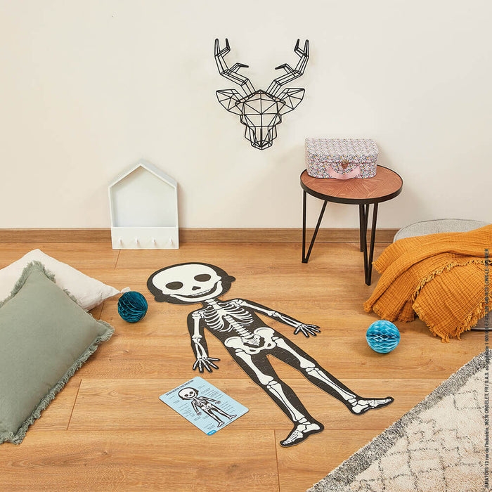 Giant black and white skeleton floor puzzle and anatomy card on wood flooring in a child's room.
