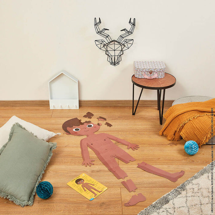 Giant anatomical floor puzzle of a boy partially built on wood flooring in a nursery with modern decor.