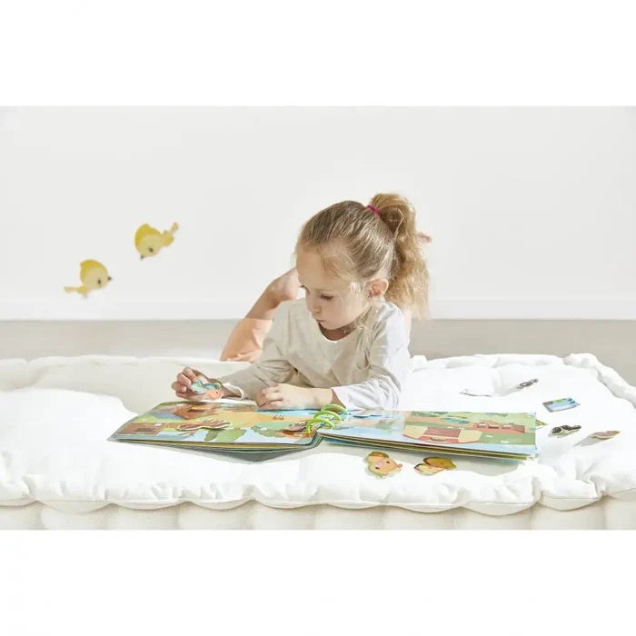 Girl on white mat playing with a spiral farm activity book featuring animal cutouts and barn illustrations.