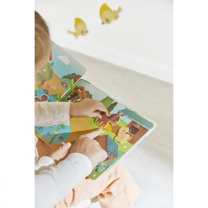 Child and adult's hands move colorful felt animal pieces on the illustrated pages of a farm-themed activity book.