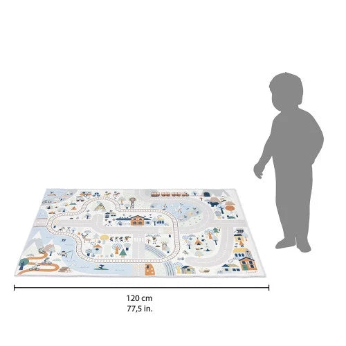 Pastel-colored rectangular play mat with a mountain village, roads, and train tracks, shown beside a child for scale.