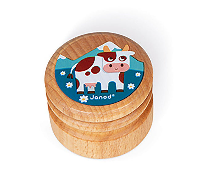 Small round wooden box with a cartoon white and brown cow illustration on a blue mountain background lid.