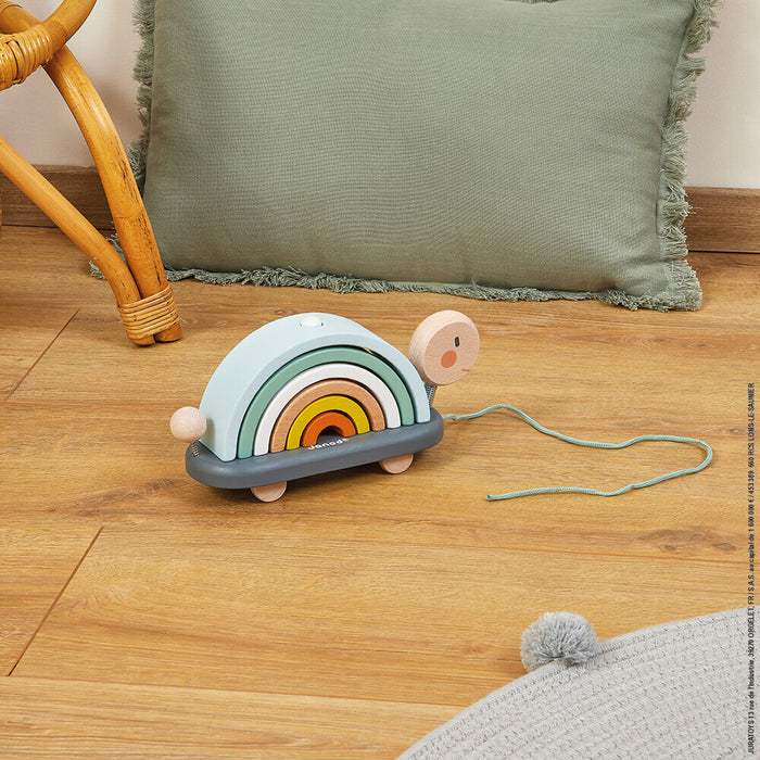 Wooden pull-along turtle with 6 colorful stacking arches for a shell, a pink head, and a blue cord on a wood floor.