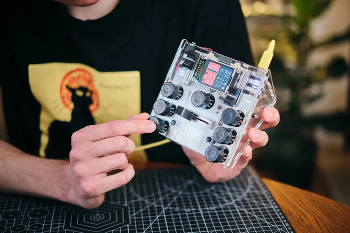 A person holding a clear acrylic DJ mixer with black knobs, a slider, and a small color digital screen.