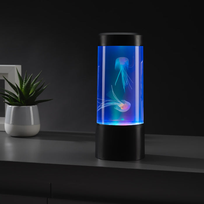 Cylindrical black lamp with blue LED light and two glowing artificial jellyfish inside, on a dark table.