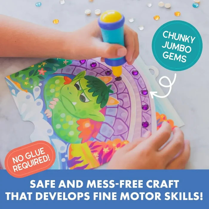 Child's hands using a blue tool to apply purple gems to a green dragon art board. Mess-free craft activity.