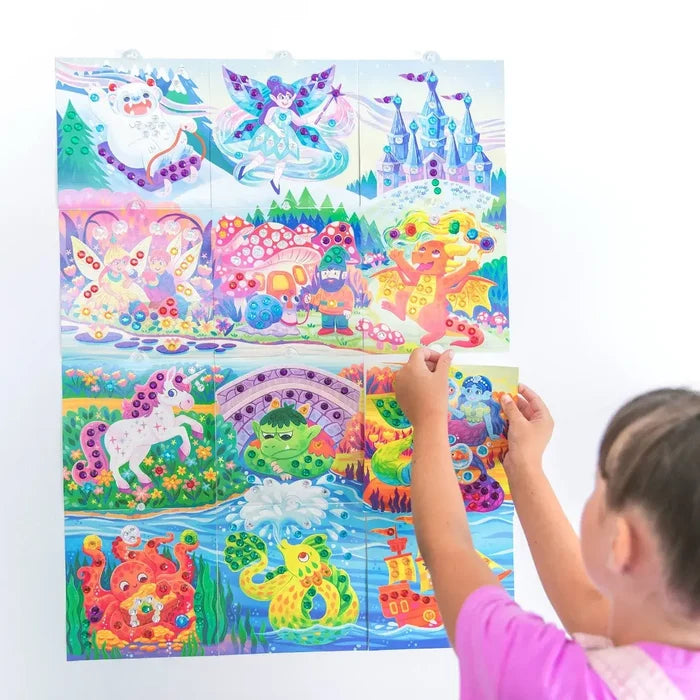 Child's hands adding a colorful gem-covered panel to a large wall mural of a unicorn, dragon, mermaid, and yeti.