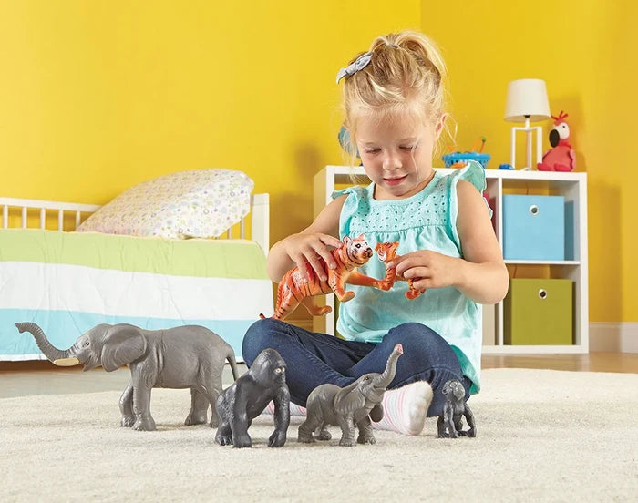 Young girl plays on a rug with pairs of large and small grey elephant, dark gorilla, and orange tiger figurines.