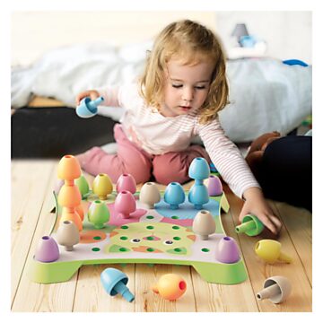 Toddler girl placing large, pastel-colored stackable pegs into a light green cat-themed pegboard.