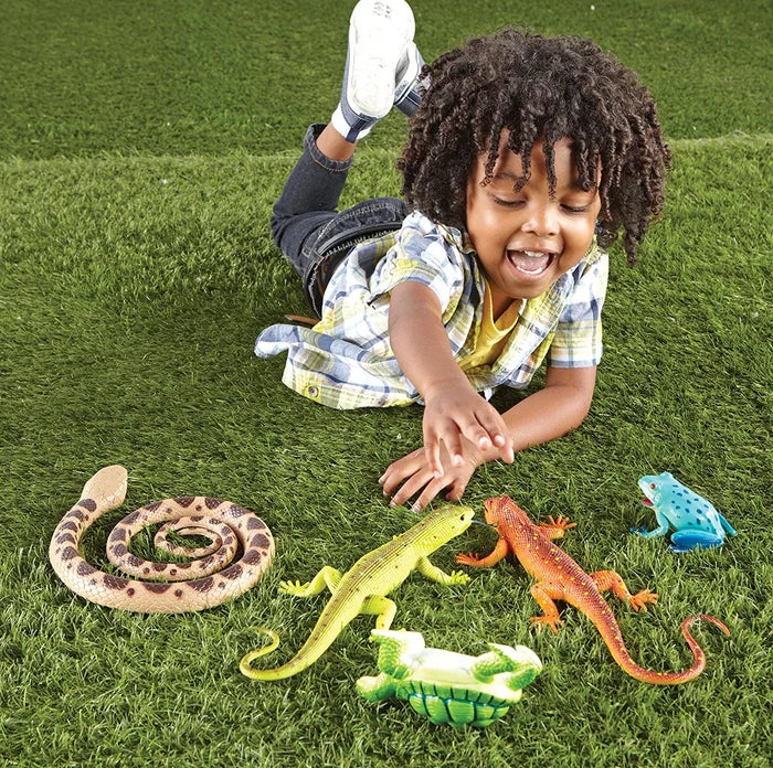 Young boy lying on grass playing with jumbo toy snake, lizards, frog, and turtle.