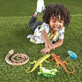 Young boy lying on grass playing with jumbo toy snake, lizards, frog, and turtle.