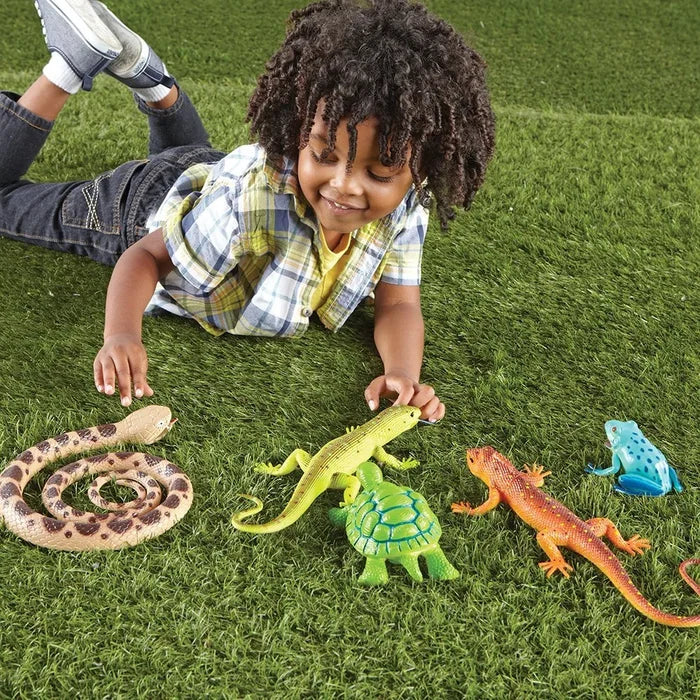 Child playing with large, colorful toy snake, lizards, turtle, and blue frog on green grass.