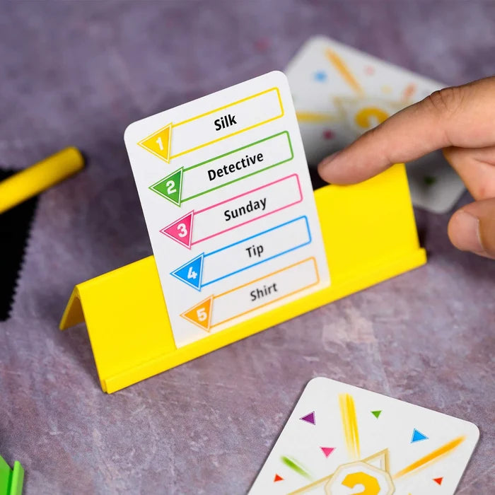 A hand points to a yellow plastic stand holding a white card listing words Silk, Detective, Sunday, Tip, and Shirt.