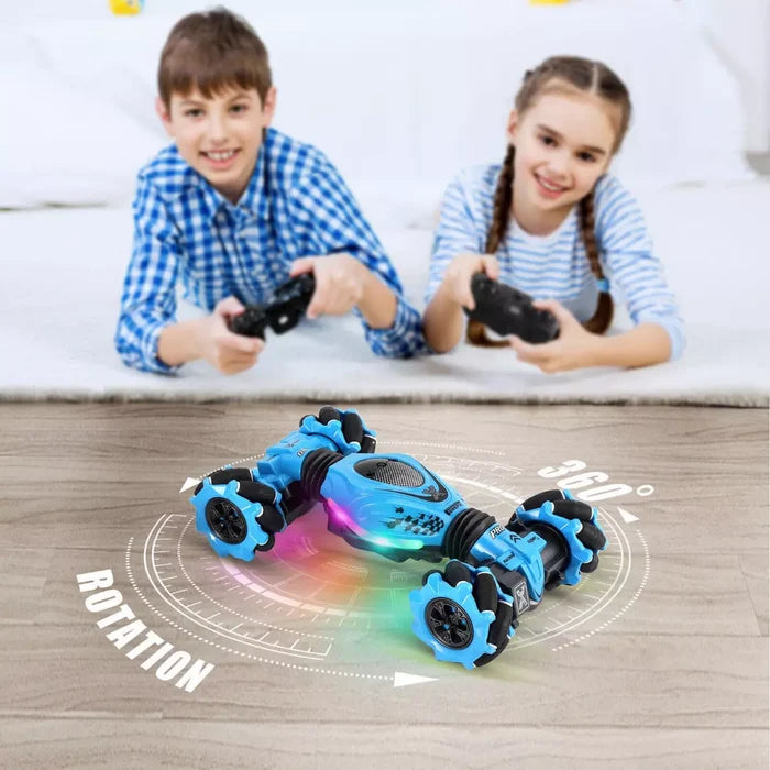 Blue light-up stunt car spins on wood floor as a boy and girl use remote controllers in the background.