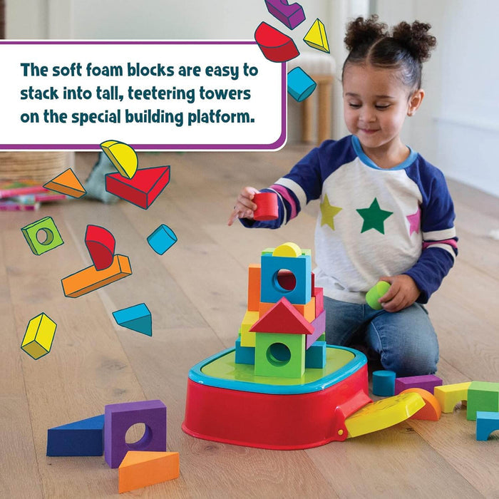 Child building a tall tower with colorful soft foam blocks on a red platform on a wooden floor.