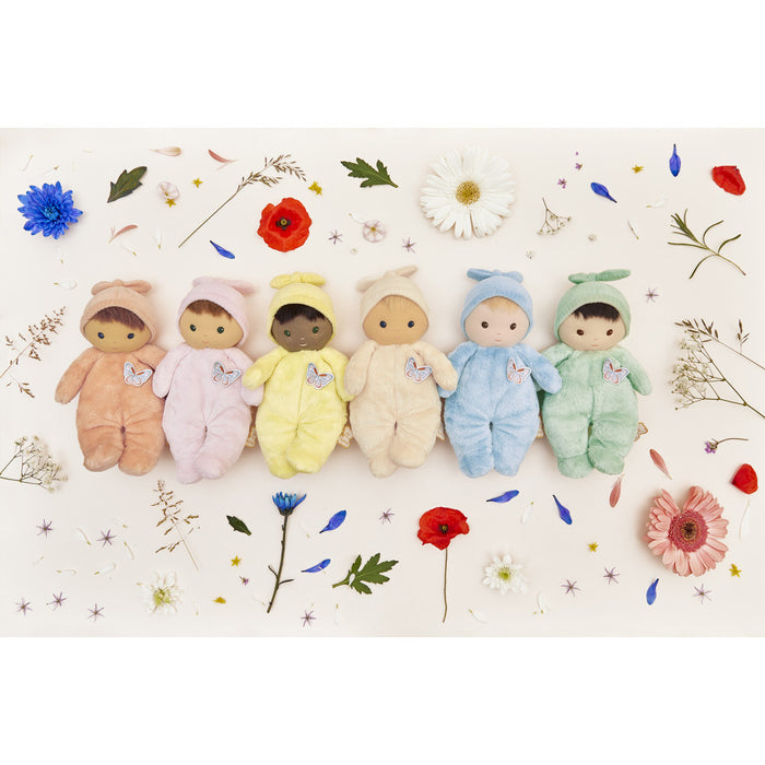 Six plush dolls in pastel hooded outfits with butterfly patches, arranged in a row among scattered colorful flowers.