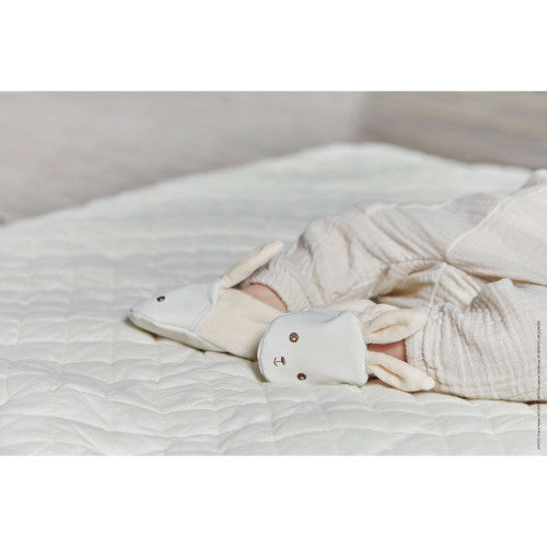 Baby feet wearing soft white plush bunny booties with embroidered faces on a white quilted blanket.