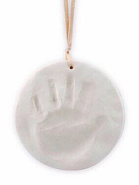 White circular plaster keepsake with a child's handprint impression, hanging from a light pink ribbon.