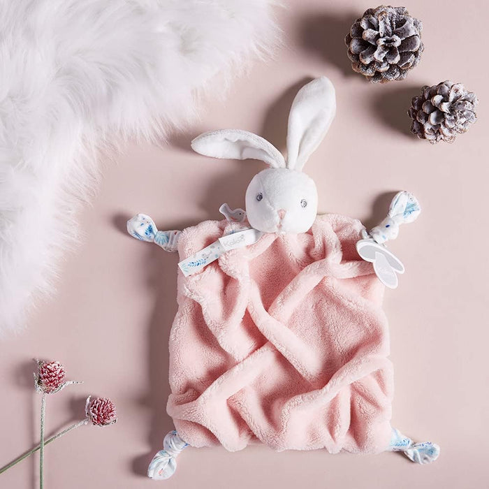 Soft white plush bunny head on a powder pink textured square baby blanket with blue patterned knotted corners.