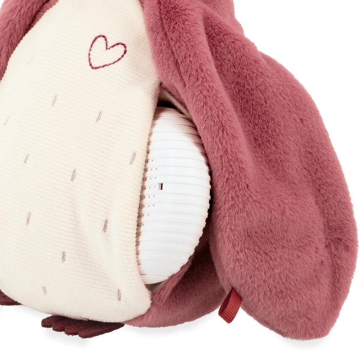 Close-up of a pink plush toy showing a white, ribbed sound device tucked into its cream-colored side pocket.