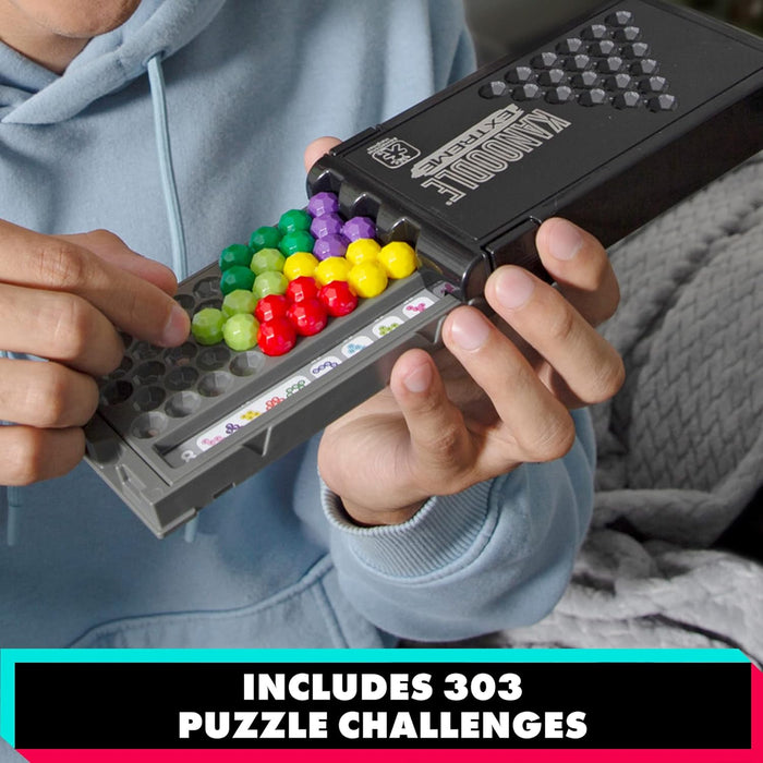 Hands place colorful sphere pieces on a grey board inside a black Kanoodle Extreme case with 303 puzzle challenges.
