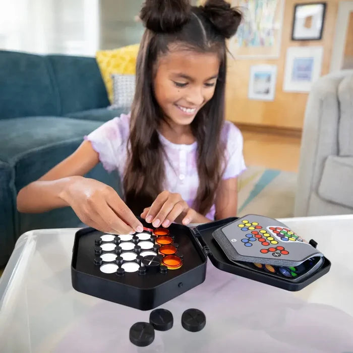 Girl playing a black hexagonal light-up puzzle game with translucent orange pieces and glowing white pegs.