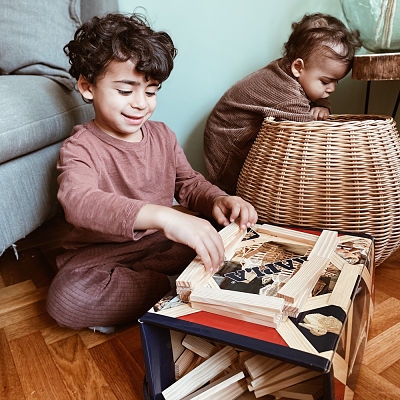 Child building a structure with flat rectangular wooden planks on top of a colorful Kapla storage box.
