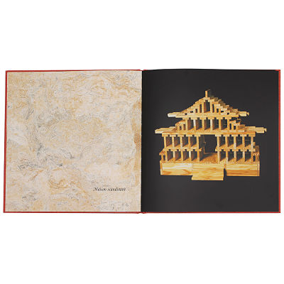 Open red book displaying a detailed wooden plank building on a black background and a marbled cream page with text.