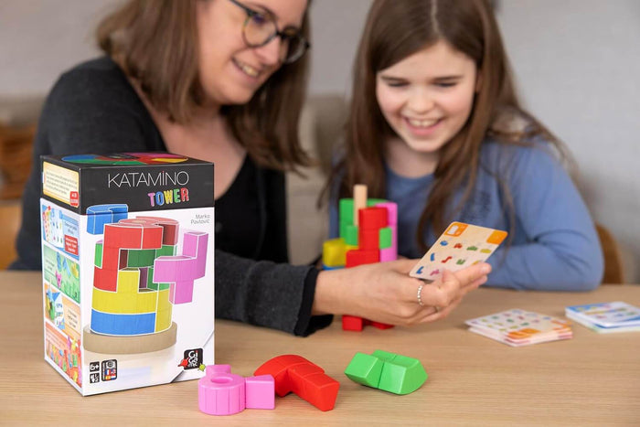 A woman and child play Katamino Tower with colorful 3D puzzle blocks and game cards on a wooden table.