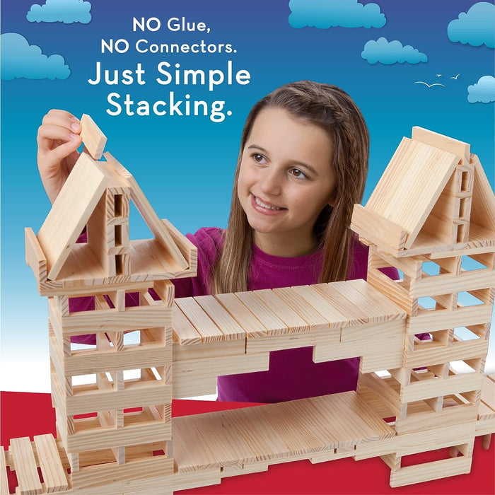 A girl stacks light-colored wooden planks to build a large bridge and towers against a blue sky background.