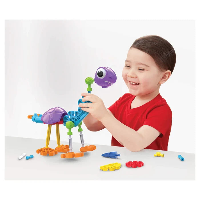 Smiling child building a colorful toy dinosaur with purple, blue, and yellow plastic pieces on a white surface.