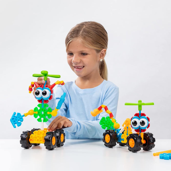 Smiling girl playing with two colorful toy characters featuring large eyes, propellers, and chunky black tires.