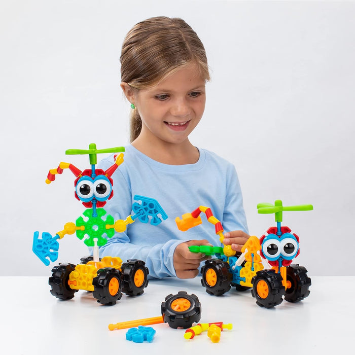 Girl smiles building colorful robot-like toys with big eyes, green propellers, and chunky wheels on a white surface.