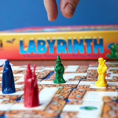 Hand reaching for colorful wizard figures on a stone maze board with a Labyrinth game box in the background.