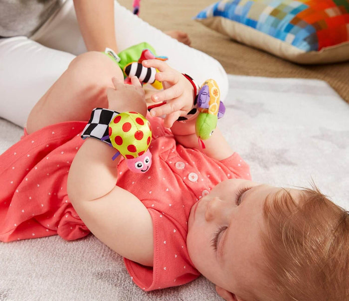 Baby lying on a star mat wearing colorful plush insect rattles with stripes and dots on their wrists and feet.