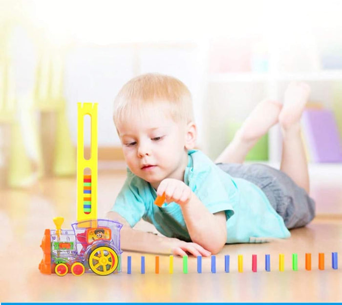Toddler playing with a transparent toy train that automatically lays a row of colorful plastic dominoes on the floor.