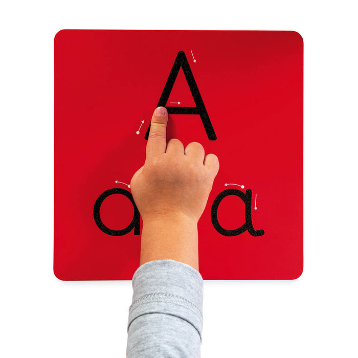 Child's hand tracing a textured black letter A on a red board with directional arrows for writing practice.