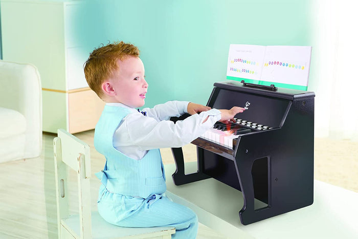 Young boy in a blue suit plays a black toy piano with light-up keys and sheet music.