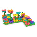 Colorful plastic gears and flower pieces interconnected on green baseplates with stems and a manual crank handle.