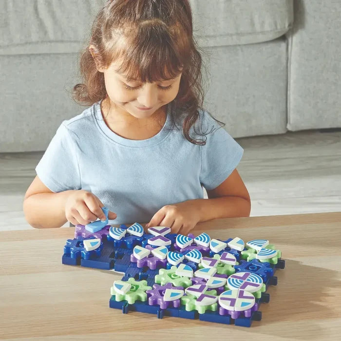 Young girl playing with interlocking green, purple, and blue gears with geometric patterns on a dark blue base.