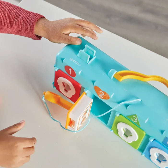 Child uses a yellow key to open a teal blue clubhouse toy featuring colorful, numbered doors with shaped locks.