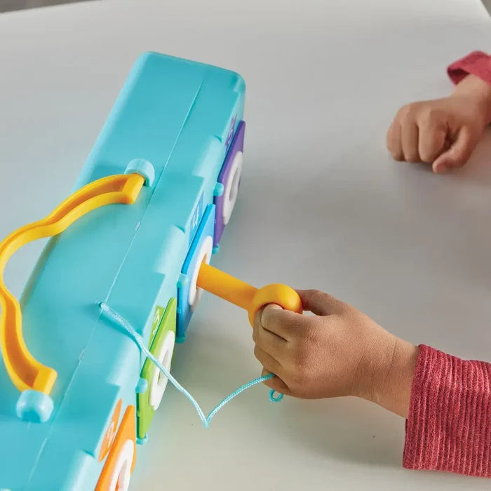 Child's hand inserting a large orange key into a blue toy clubhouse with colorful numbered doors and a yellow handle.