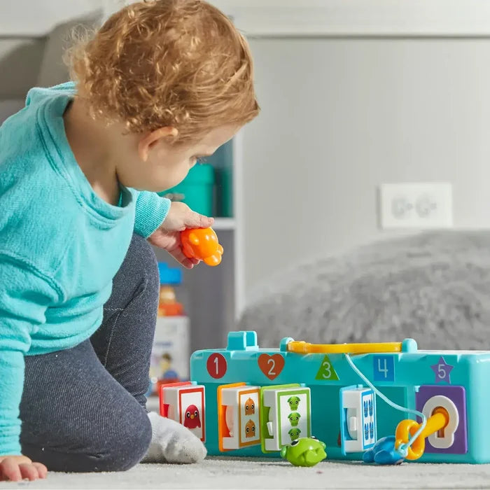 Toddler playing with a blue toy featuring five numbered doors with colorful shapes and matching animal keys.